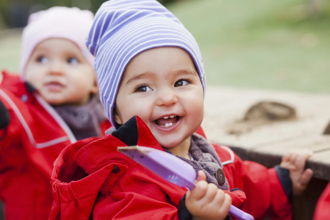 A smiling toddler exploring outdoor play with a toy shovel